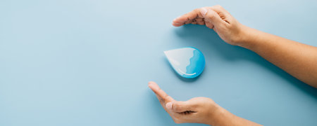 World Water Day. Two hands cradle a blue water drop paper cut, symbolizing water care, hygiene, and saving each precious drop for a cleaner world and sustainable environment. CSRの写真素材