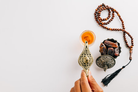 Ramadan flat lay with tea, dates, and prayer beads on a white background. A hand pours tea from a teapot, embodying holy traditions and a serene celebration. Ramadan dayの写真素材