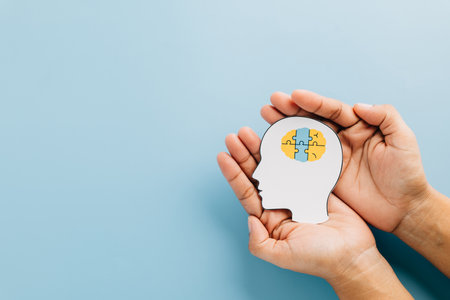 Down Syndrome Day concept with hands holding a brain jigsaw in a head cutout. Spreading awareness of Down Syndrome and Autism Awareness worldwide on a blue background.の写真素材