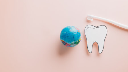Paper tooth, toothbrush, and world on pastel pink for Dentist Day. Celebrate oral hygiene, dental care, and health with flat lay visuals emphasizing global dental awareness.の写真素材