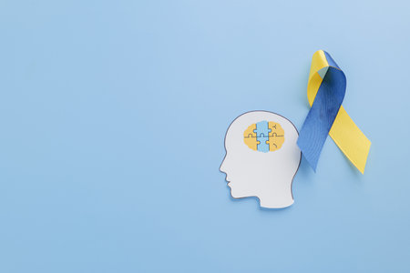 Paper head with puzzle pieces forming a brain and a yellow-blue ribbon highlights Down Syndrome awareness. Supporting World Down Syndrome Day on a blue background.の写真素材