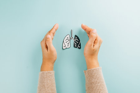 World TB Day concept with two hands cradling lungs paper on blue background. Highlighting lungs health, tuberculosis awareness, and the prevention of respiratory diseases like COPD and pneumonia.の写真素材