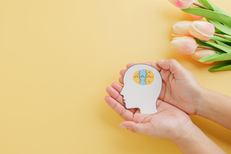 Brain jigsaw in head paper cut held by hands on yellow background marks World Down Syndrome Day. Promoting Down Syndrome awareness and Autism Awareness worldwide.の写真素材