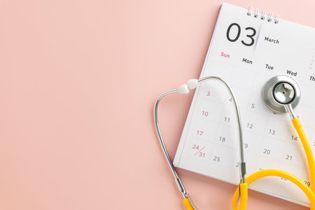 Yellow stethoscope with calendar on pink for Doctor Day concept. Promoting medical awareness, health exams, annual checkups, and appointment reminders.の写真素材