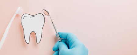 Tooth, toothbrush, and mirror held by a gloved hand on pink. A Dentist Day concept highlighting...