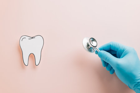 Paper tooth, gloved hand with stethoscope on pink for Dentist Day. Highlighting dental care, medical imagery, and oral health awareness in a creative flat lay design for healthcare themes.の写真素材