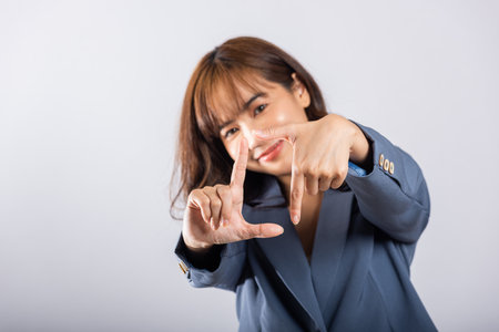 Portrait of a happy young business woman framing with her finger in front of her face, capturing the concept of photography. Studio shot on white backgroundの写真素材