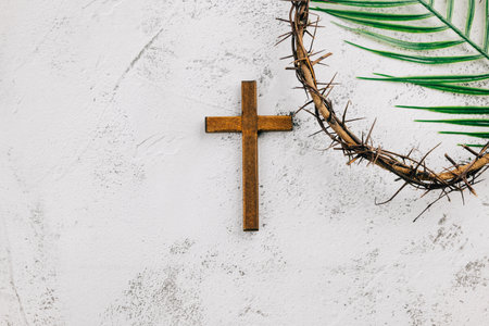 Crown of thorns with wooden cross and palm leaves on gray background. Symbolic of Palm Sunday...
