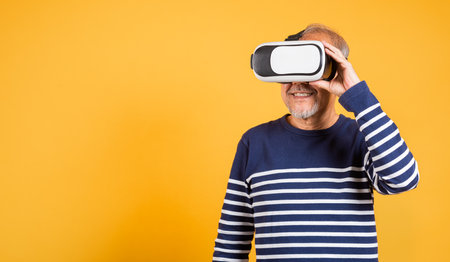 Portrait Asian smiling old man holding in a virtual reality glasses headset studio shot isolated yellow background, Excited happy senior man pensioner using VR play simulation gameの写真素材