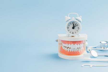 Dentist Day. A Dentist arranges a teeth model, stethoscope, tools, and a white alarm clock on a blue...
