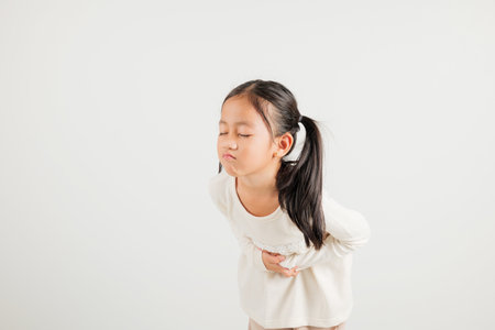 Portrait of Asian young kid girl has stomachache, kindergarten child abdominal pain suffering from stomach ache, studio shot isolated on white background, food poisoning, Health and medical gastritisの写真素材