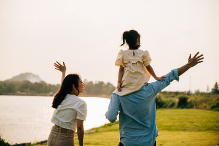 Asian family child girl piggyback riding back on father raising hands like flying outdoor nature park with mother, Happy parent daughter having fun together, Tourist lifestyle family leisure activityの写真素材