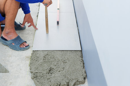 A detailed view of a worker leveling gray mortar with a tool, preparing for the placement of floor tiles in a house construction project.の写真素材