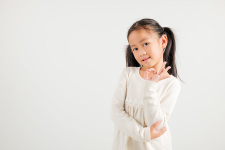 Exuberant young kid girl showcases the OK sign with an optimistic smile, conveying agreement and positivity isolated on a white background, ideal for your text customization. kindergarten child smileの写真素材