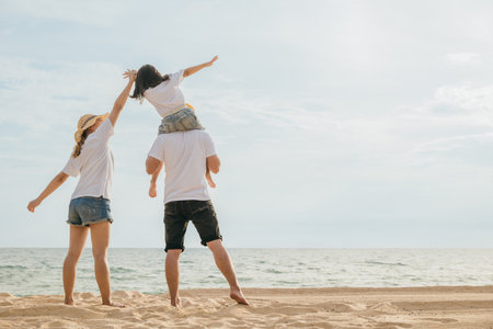 Happy family in holiday. Father, Mother and kids having fun together shoulder ride on summer beach, Parents carrying children on neck at beach, family is enjoying their summer timeの写真素材
