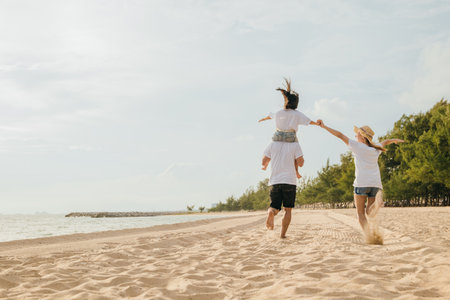 Happy family in holiday. Father, Mother and kids having fun together shoulder ride and running on summer beach, Parents carrying children on neck, family is enjoying their summer in sunset timeの写真素材