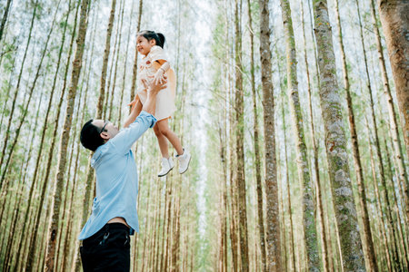 Playful family moment, father holds happy little girl up high, throwing up in sky at park forest. cheerful child enjoy moment playing freedom and joy, while loving dad captures precious memory foreverの写真素材