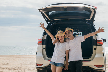Asian couple is posing in back of a car enjoying beautiful views on the ocean beach. lifestyle man and the woman is wearing hat. Scene is relaxed and carefree, love and travel summer trip conceptの写真素材