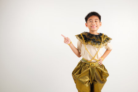 Portrait Thailand kid boy smiling traditional Thai dress costume indicate finger empty space, studio isolated white background, primary child pointing index out with copy spaceの写真素材