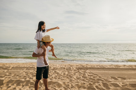 Happy family in holiday. Father and kids having fun together shoulder ride on summer beach, Parents carrying children on neck at beach, family is enjoying their summer in sunset timeの写真素材