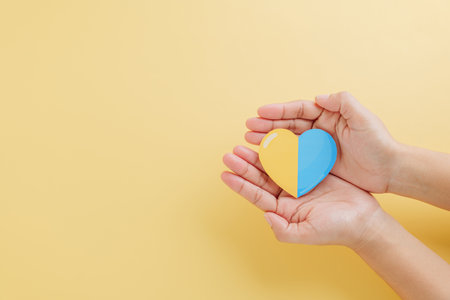 Down Syndrome Day. Two hands hold a divided heart, yellow and blue, on a yellow background. Raising awareness for Down Syndrome and Autism Awareness globally.の写真素材