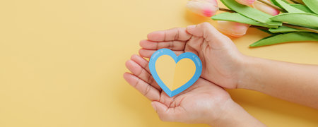 Yellow and blue heart held by hands on a yellow background for Down Syndrome Day. Raising awareness...