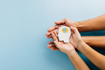 Adult and child hands hold a brain jigsaw in a head paper cut for Down Syndrome awareness. Highlighting global Down Syndrome Day and Autism Awareness with care and support.の写真素材