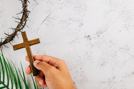 Palm Sunday focus, hand holds wooden cross and thorns crown on textured white background. Symbolizing Easter and spiritual reflection.の写真素材