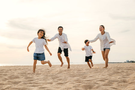 Cheerful family with happy parents and children running on the beach. Summer holiday joy captured in a snapshot of laughter play and smiles. Carefree moments of family bonding and relaxation.の写真素材