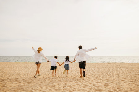 On the beach a family in full vitality parents holding hands running with their children and joyfully jumping in holiday freedom. Capturing the spirit of family travel and beach vacation enjoyment.の写真素材