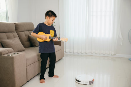 Child stands playing a ukulele in a stylish living room. His cheerful demeanor and the cozy interior convey a sense of joy, creativity, and the charm of childhood.の写真素材