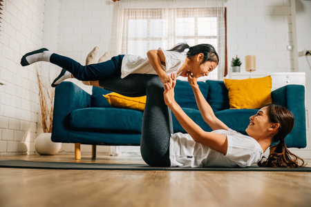 In a heartwarming family yoga session at home a mother and her daughter joyfully practice flying like airplanes cultivating trust harmony and happiness in their special relationship.の写真素材