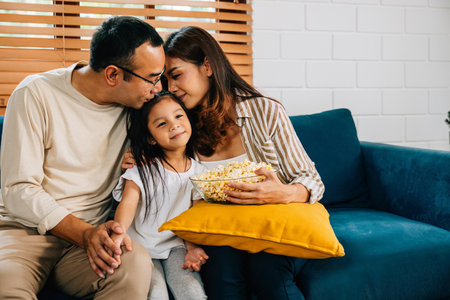In heart their cozy home joyous family enjoys TV time with popcorn. father mother daughter and sibling are all smiles creating precious memories of togetherness and bonding during their quality time.の写真素材