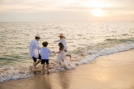 Spectacular sunset setting at beach showcasing parents and kids enjoying holiday together. blissful summer vacation scene with happy mother father and children running in ocean creating cherishedの写真素材