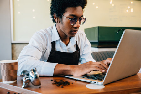 Manager and barista inspecting coffee beans on laptop in clean modern roastery. Using technology and calculator ensuring quality. Business owner at work verifying beans a precise check is key.の写真素材