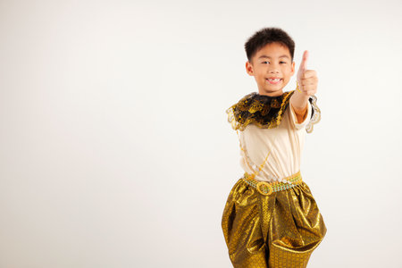 Portrait Thailand kid boy smiling traditional Thai dress costume makes thumbs up OK sign, symbolizing agreement, studio isolated white background, primary child radiates positivity and satisfactionの写真素材