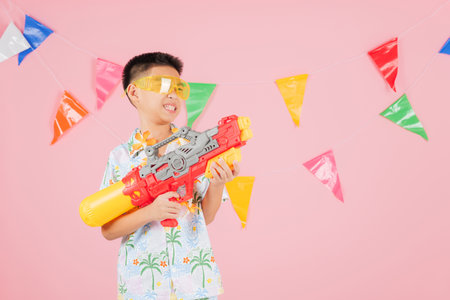 Songkran festival fun A happy child in glasses and a bright floral shirt holds a water gun, ready...