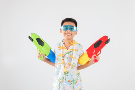 Songkran excitement as a cheerful kid child in glasses holds two toy water guns Songkran in Thailand is a joyful festival filled with playful splashes and tradition. isolated white backgroundの写真素材