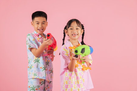 Songkran fun as a cheerful Thai boy and girl hold toy water pistols together, celebrating the exciting culture of Songkran in Thailand, isolated pink backgroundの写真素材