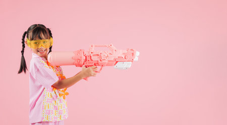 Songkran festival happiness as a joyful girl in glasses and a floral outfit holds water gun, capturing the festive atmosphere of Songkran in Thailand with a cheerful smile isolated on pink backgroundの写真素材