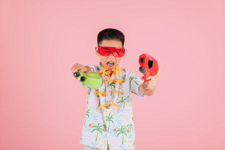 Songkran brings joy as a smiling kid in a floral shirt and glasses holds two water toys, celebrating Songkran traditions in Thailand isolated against a colorful pink backgroundの写真素材