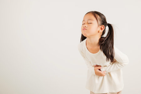Portrait of Asian young kid girl has stomachache, kindergarten child abdominal pain suffering from stomach ache, studio shot isolated on white background, food poisoning, Health and medical gastritisの写真素材