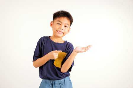 Asian happy portrait cute young boy smile presenting product holding something on palm away side, studio shot isolated on white background with copy space, primary child show hand gestureの写真素材