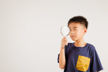 Asian little kid boy funny looking through magnifying glass at studio shot isolated on white background, Happy primary child lifestyle smiling exploring holding magnifier searching, Educationの写真素材