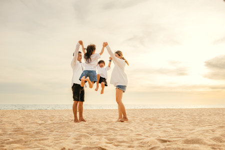 Beachside celebration as an Asian family with father and mother holding children jumps joyfully into air. beautiful ocean background captures essence of family happiness and carefree fun.の写真素材