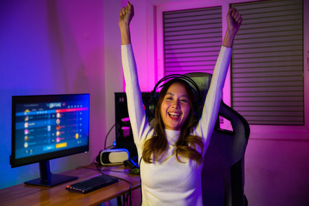 Winning Victory. Asian gamer playing online video game excited on desktop computer PC colorful neon LED lights, young woman in gaming raise hand to enjoying happy successful, E-Sport, front viewの写真素材