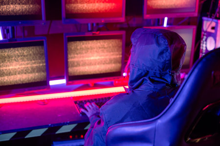 Woman hacker wear hood sit front computer typing on keyboard in neon light, Gamer woman streaming game online dark room, Female hacker in data center, Cyberattackの写真素材