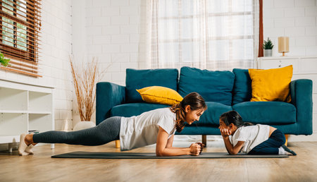 In a cozy atmosphere a mother and her charming daughter practice family yoga stretching and balancing together. Their smiles showcase a happy and harmonious family moment.の写真素材