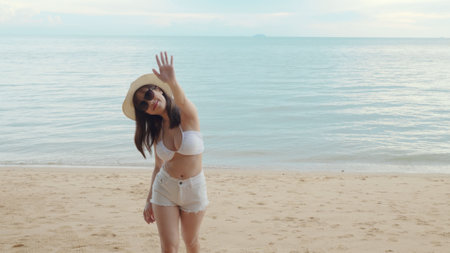 Beautiful Asian woman wear sunglasses and hat turning back running to tropical paradise beach, Happy female in bikini having fun with hand to camera inviting you come with meの写真素材