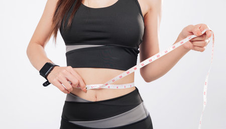 Tape for tracking and tape for success, this smiling woman in sport attire proudly measures her slim waist, celebrating weight loss and healthy living. isolated studio white backgroundの写真素材